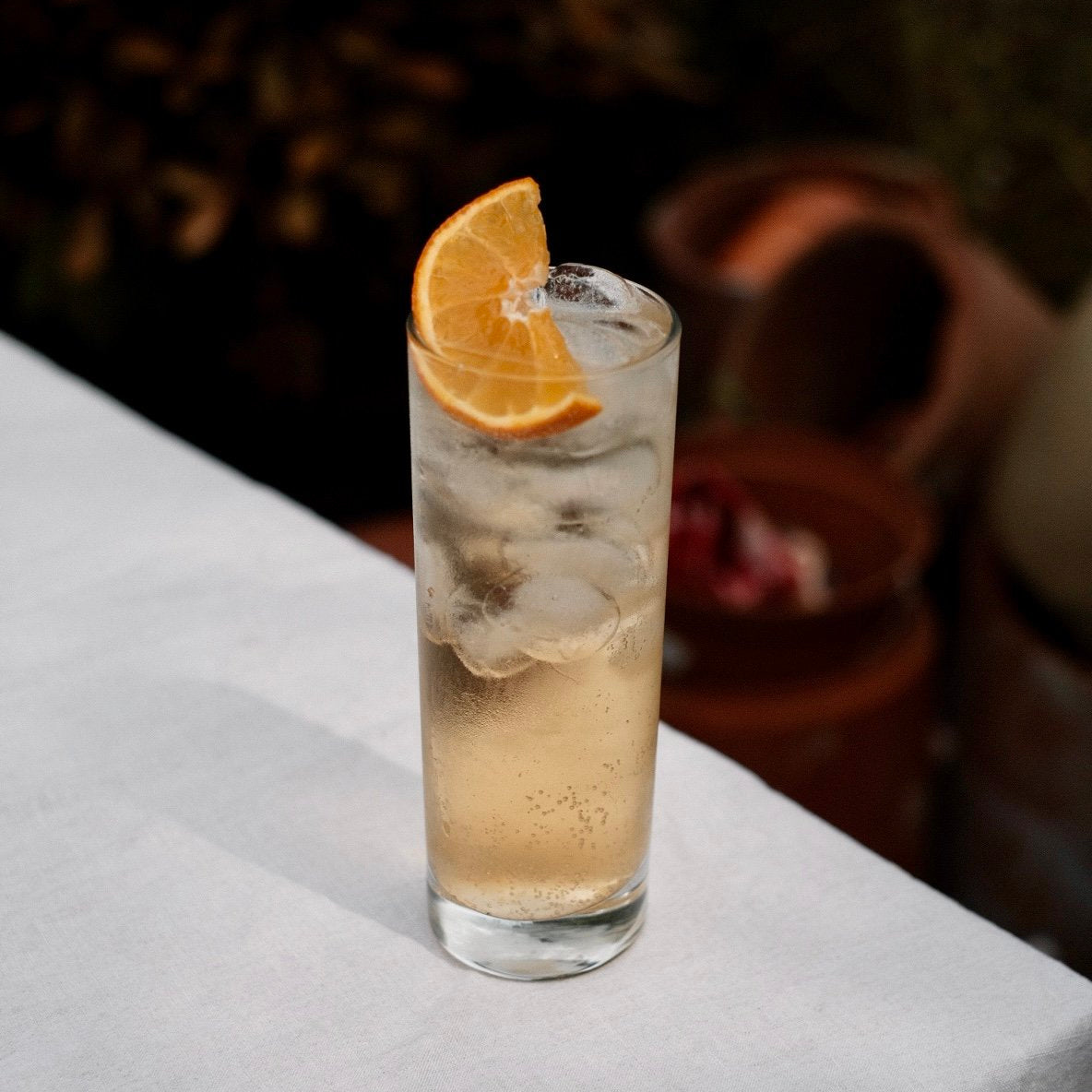 Tall glass of iced golden spiced rum highball garnished with an orange wedge, served outdoors at Loveday Distillery