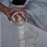 Hand holding a coupe glass of pale Kissing Gate Gin cocktail, second glass on white linen surface, Cornwall