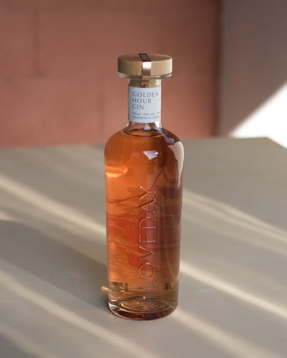 Loveday Distillery Golden Hour Gin bottle with warm amber liquid, wood cap, white label, soft pink background