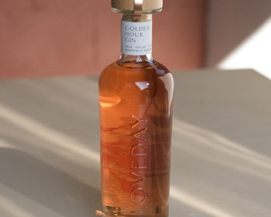 Loveday Distillery Golden Hour Gin bottle with warm amber liquid, wood cap, white label, soft pink background
