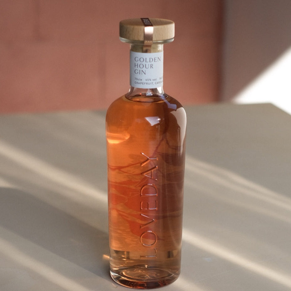 Loveday Distillery Golden Hour Gin bottle with warm amber liquid, wood cap, white label, soft pink background