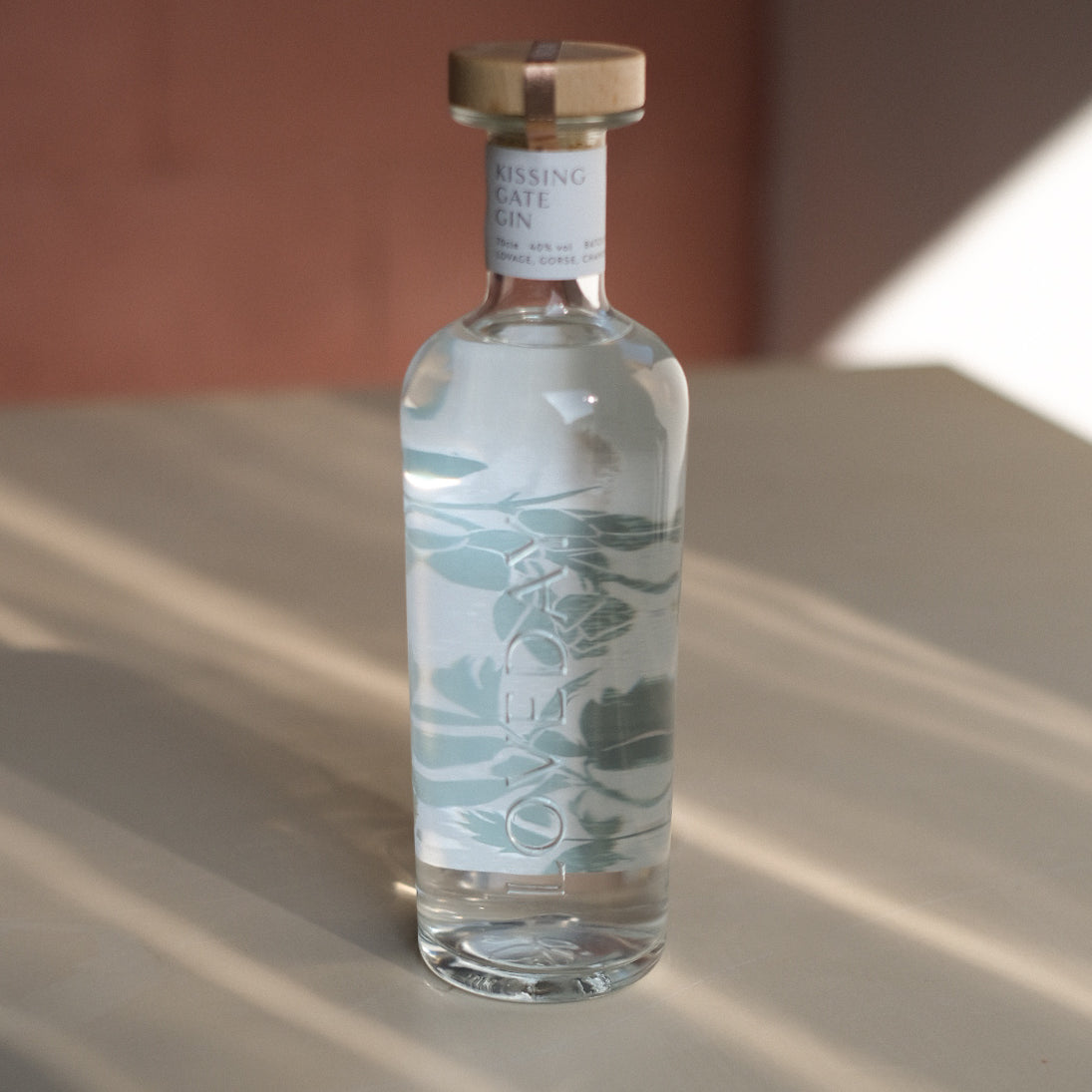 Kissing Gate Gin bottle with sage botanical illustration and wooden cap, photographed in warm natural light