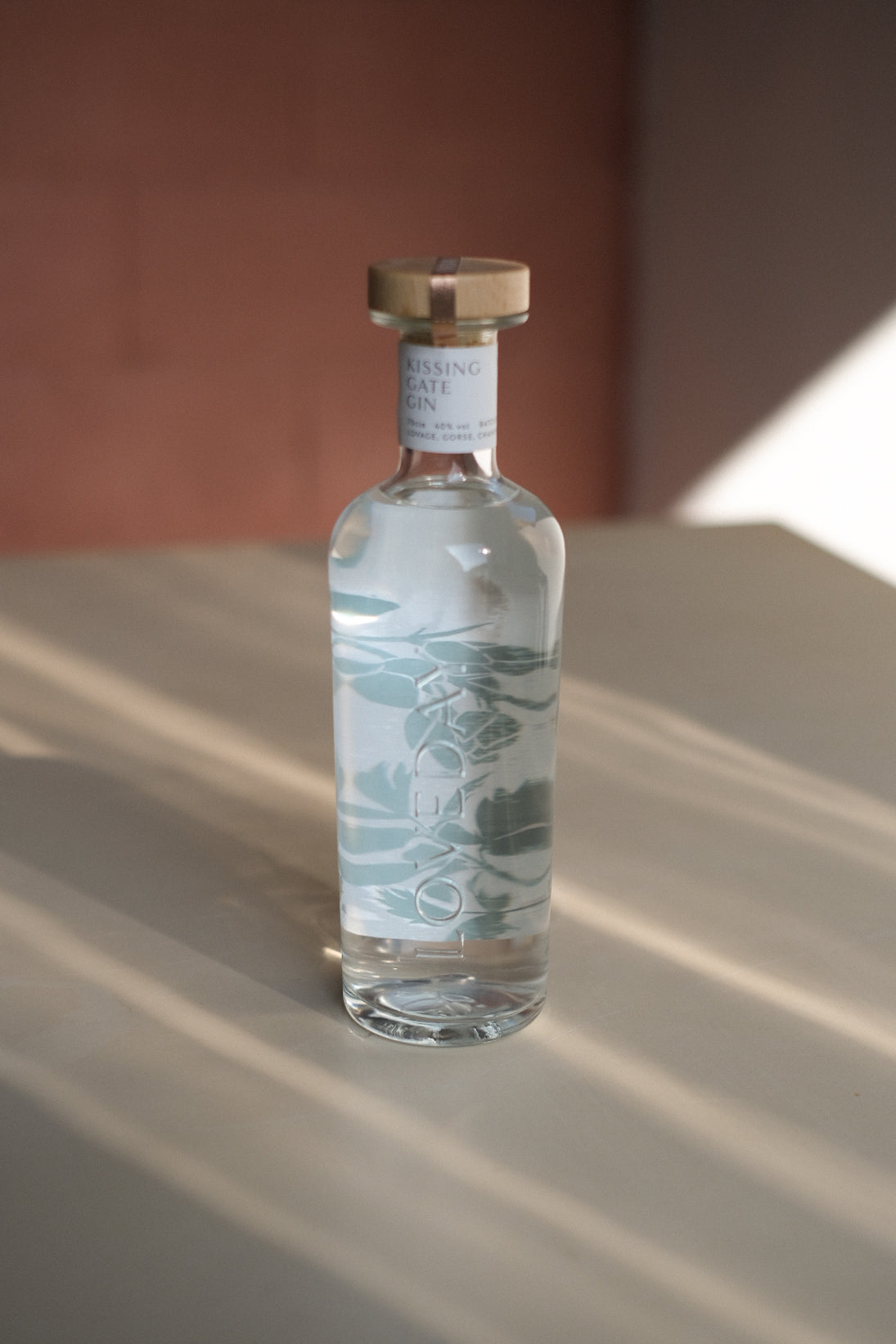 Kissing Gate Gin bottle with sage botanical illustration and wooden cap, photographed in warm natural light