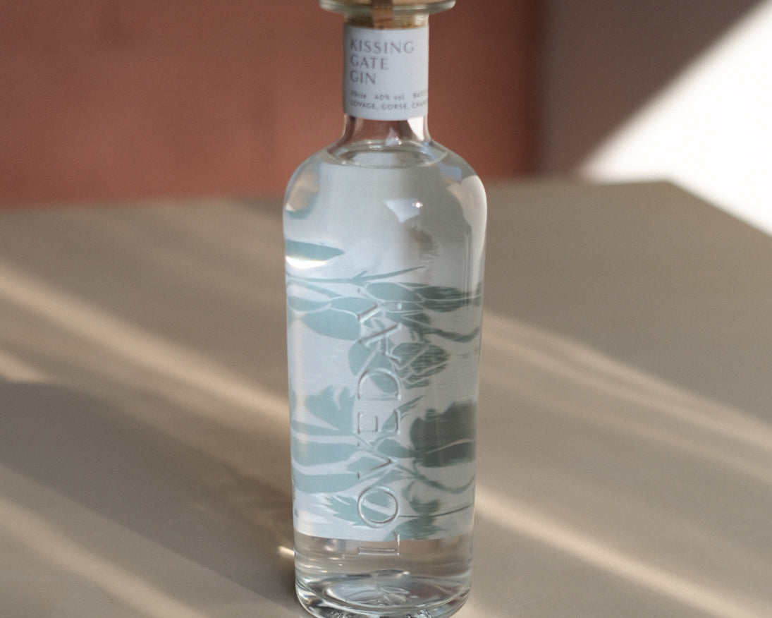 Kissing Gate Gin bottle with sage botanical illustration and wooden cap, photographed in warm natural light