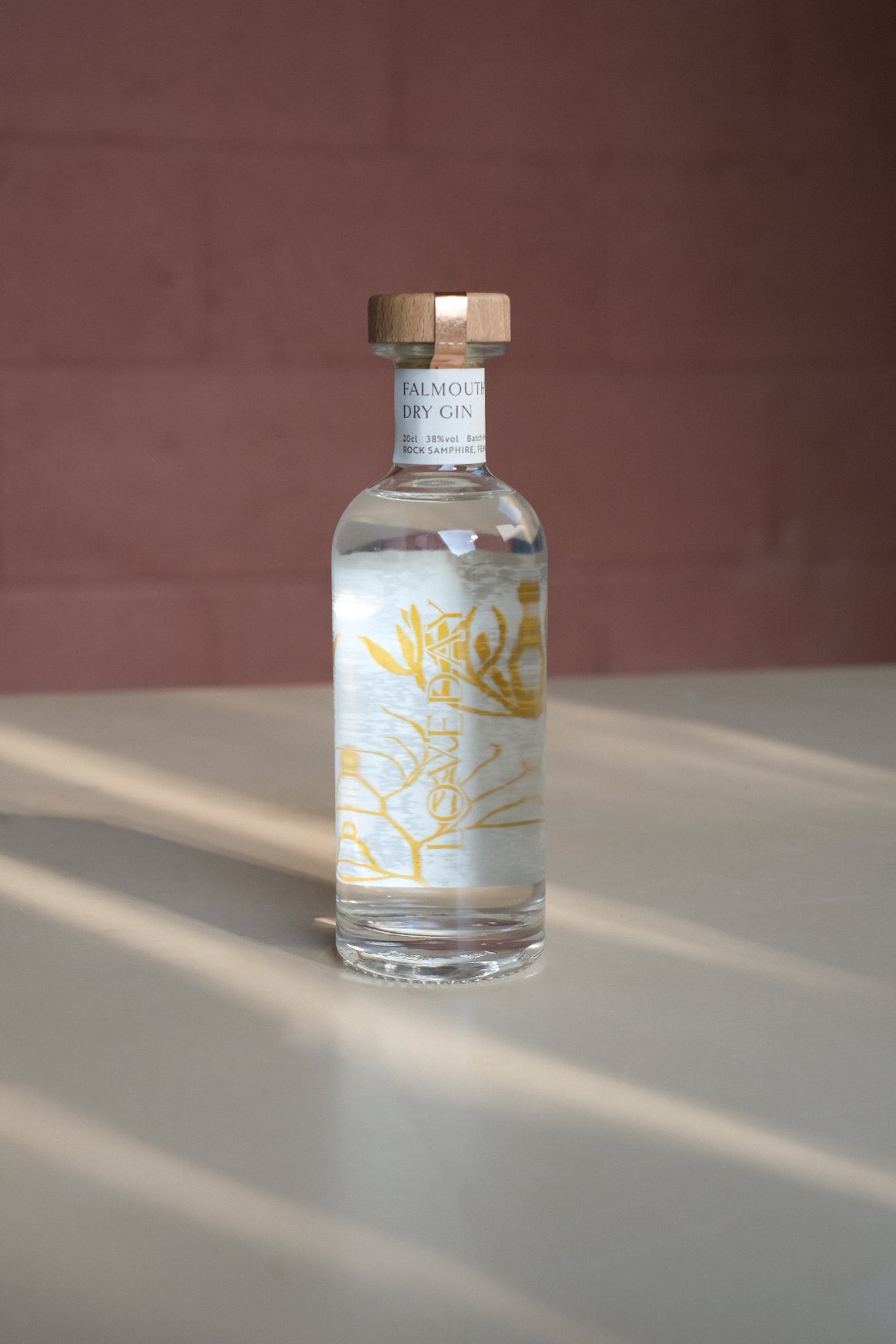 Falmouth Dry Gin 20cl bottle by Loveday Distillery with golden botanical label and wooden cap, lit by warm sunlight