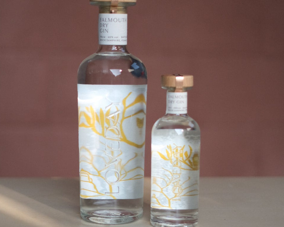 Two Loveday Falmouth Dry Gin bottles, large and mini, clear glass with gold botanical labels and copper caps