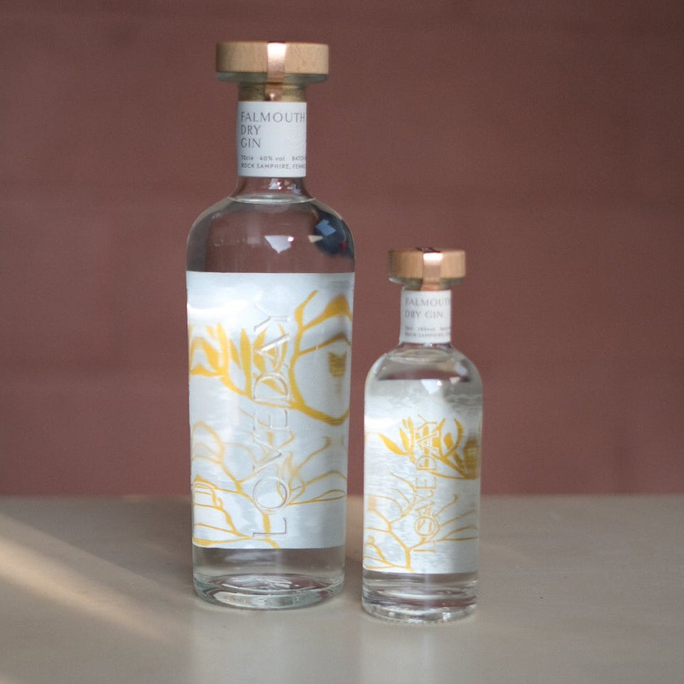 Two Loveday Falmouth Dry Gin bottles, large and mini, clear glass with gold botanical labels and copper caps
