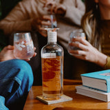 Loveday Golden Hour Gin bottle on wooden table, friends sharing grapefruit gin in stemless glasses at a cosy gathering