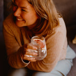 Woman smiling, holding a Loveday stemless glass with ice and a citrus slice in warm golden light