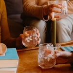 Friends holding Loveday stemless glasses with iced gin cocktails and citrus garnish around a candlelit wooden table