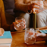 Friends holding Loveday stemless glasses with iced gin cocktails and citrus garnish around a candlelit wooden table