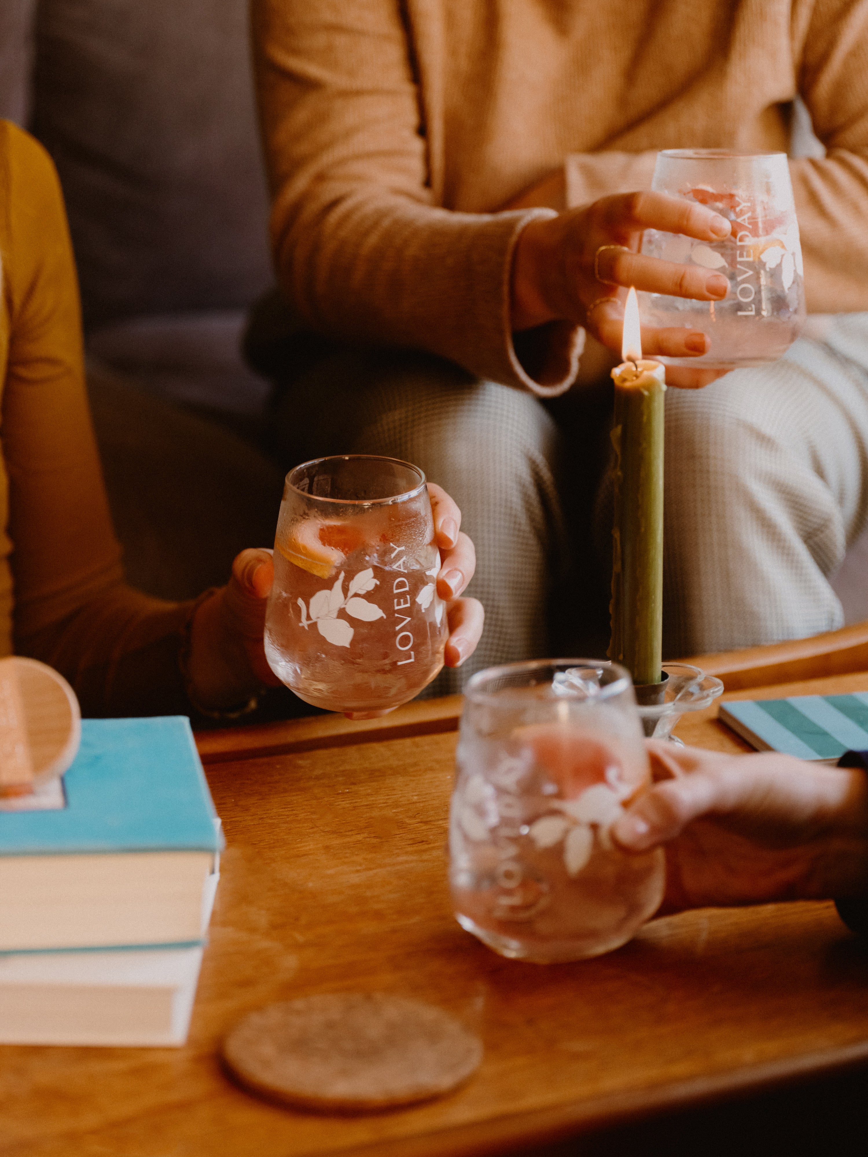 Friends holding Loveday stemless glasses with iced gin cocktails and citrus garnish around a candlelit wooden table