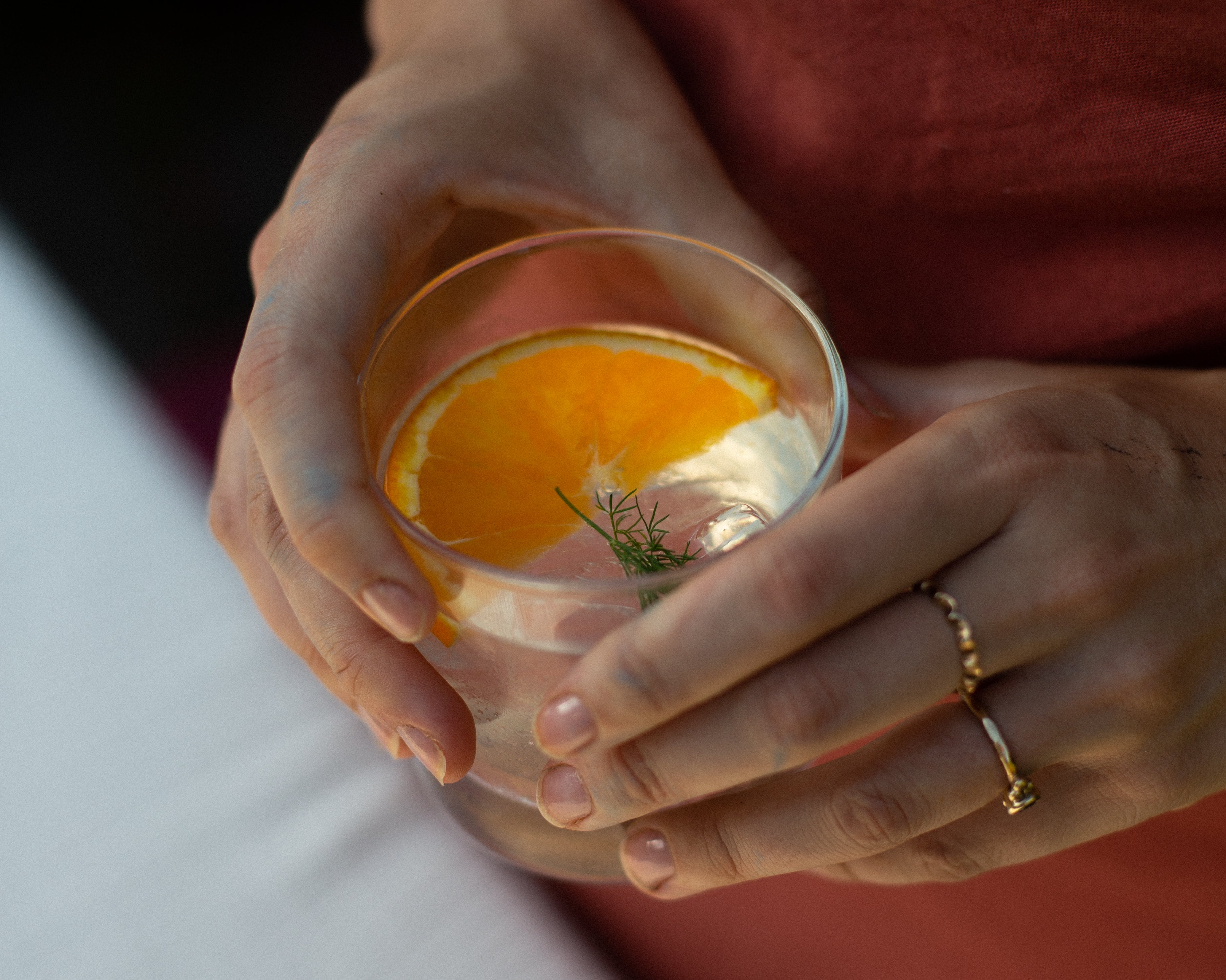 Hands cradling a rocks glass with an orange slice and dill garnish, Loveday Distillery Falmouth Dry Gin serve