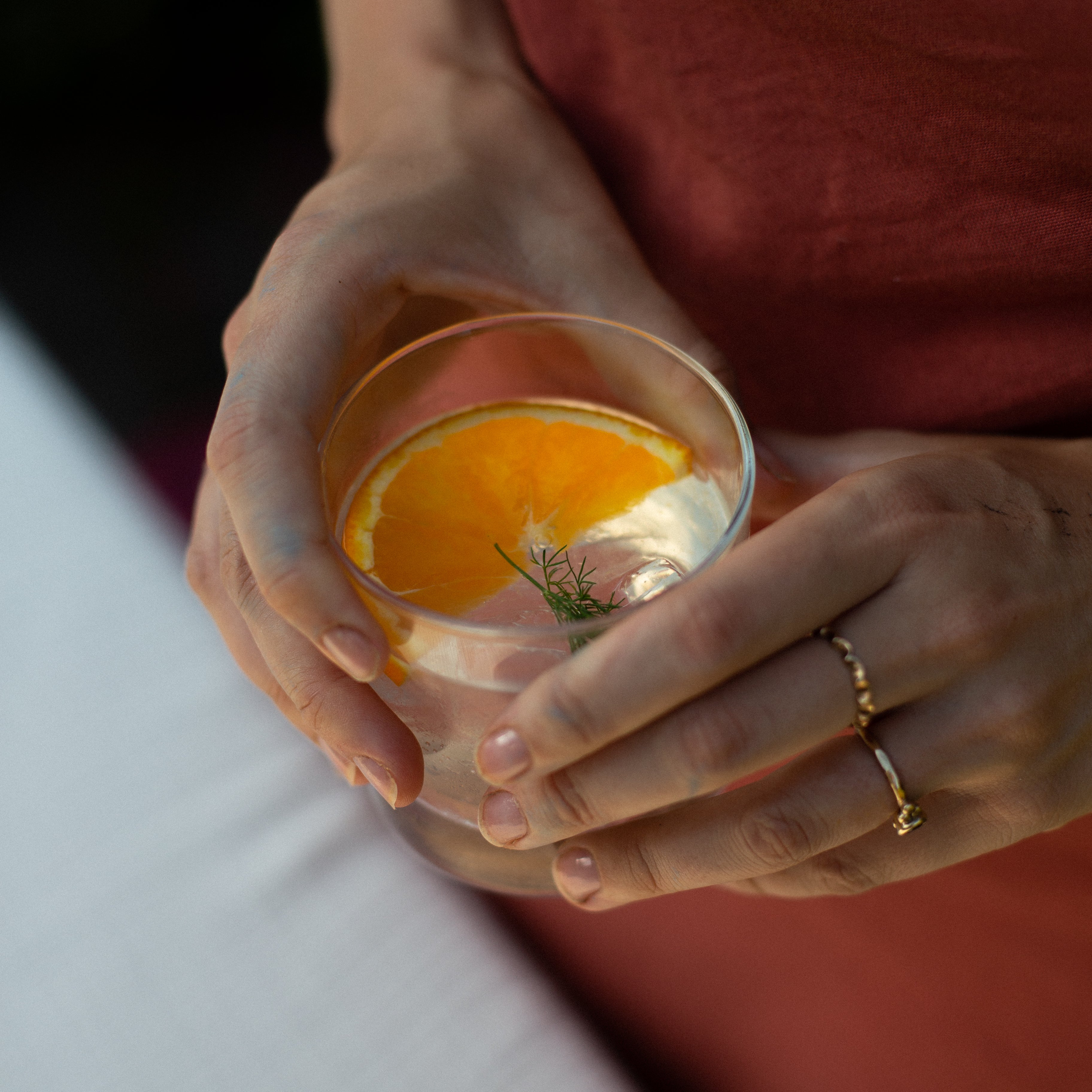Hands cradling a rocks glass with an orange slice and dill garnish, Loveday Distillery Falmouth Dry Gin serve
