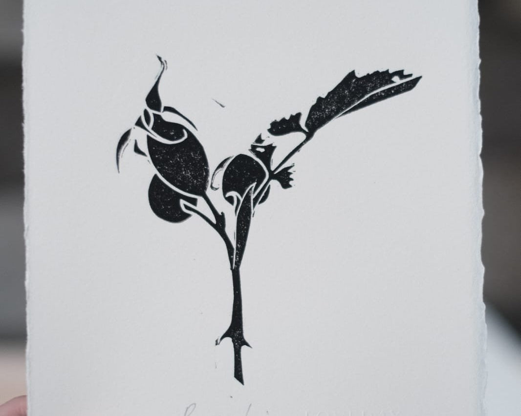 Black lino print of rosehip branch with berries and leaves on deckle-edged paper, titled Rosehip Loveday