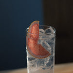 Tall glass of gin and tonic over ice with a pink grapefruit wedge garnish, served at Loveday Distillery