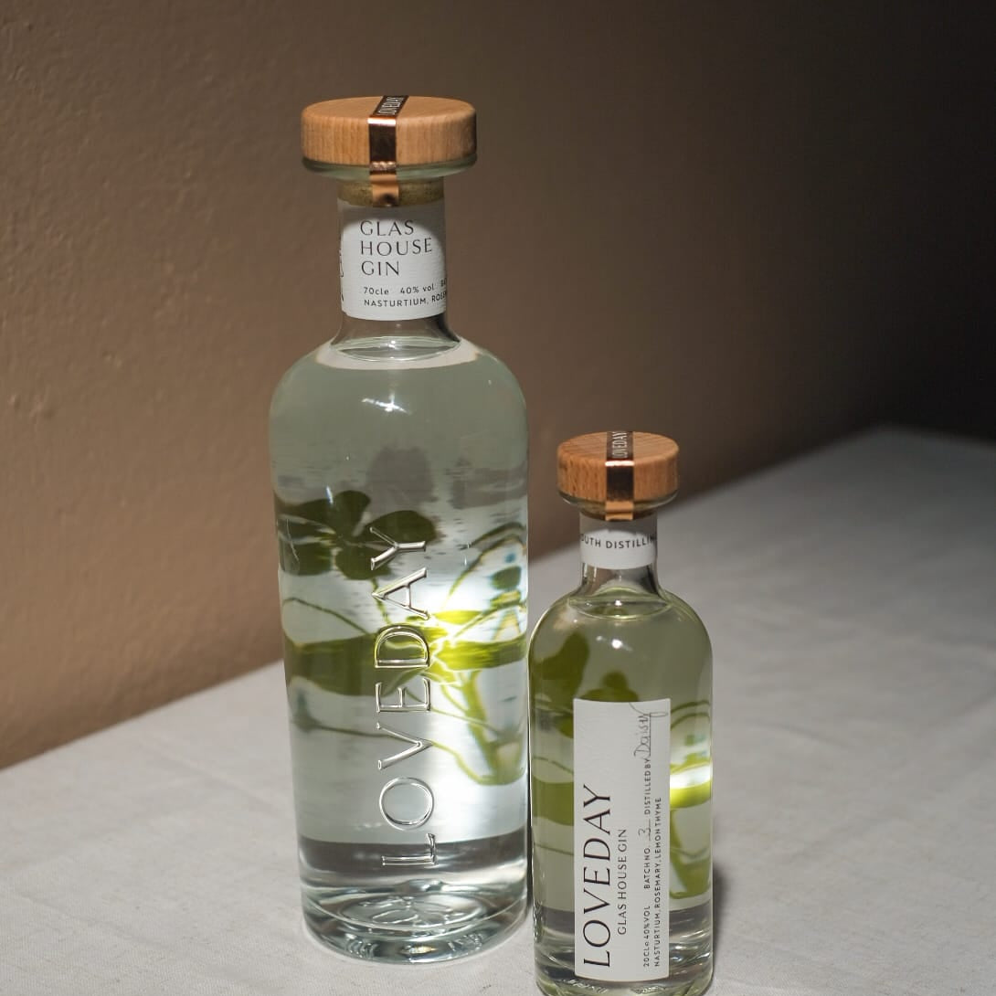 Two clear glass bottles of Loveday Glas House Gin with botanical illustrations and wooden caps, large and miniature sizes