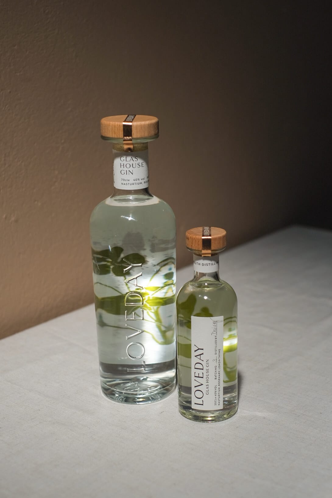 Two clear glass bottles of Loveday Glas House Gin with botanical illustrations and wooden caps, large and miniature sizes