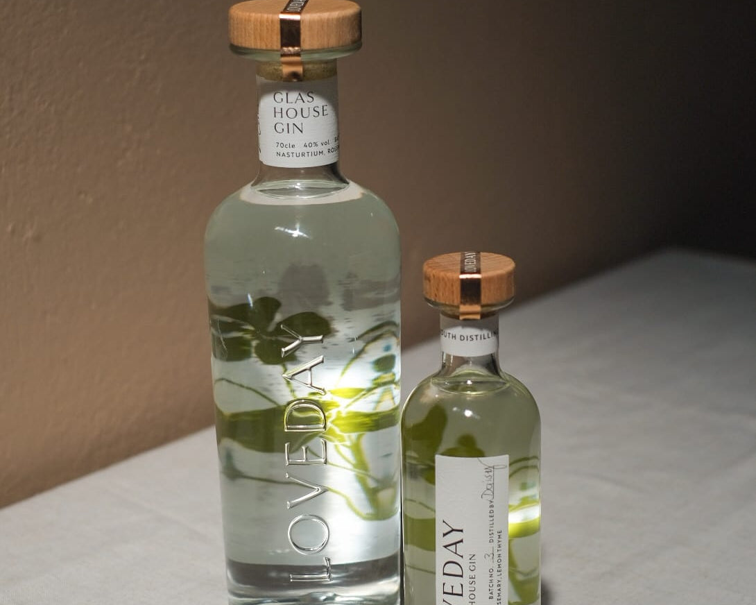 Two clear glass bottles of Loveday Glas House Gin with botanical illustrations and wooden caps, large and miniature sizes