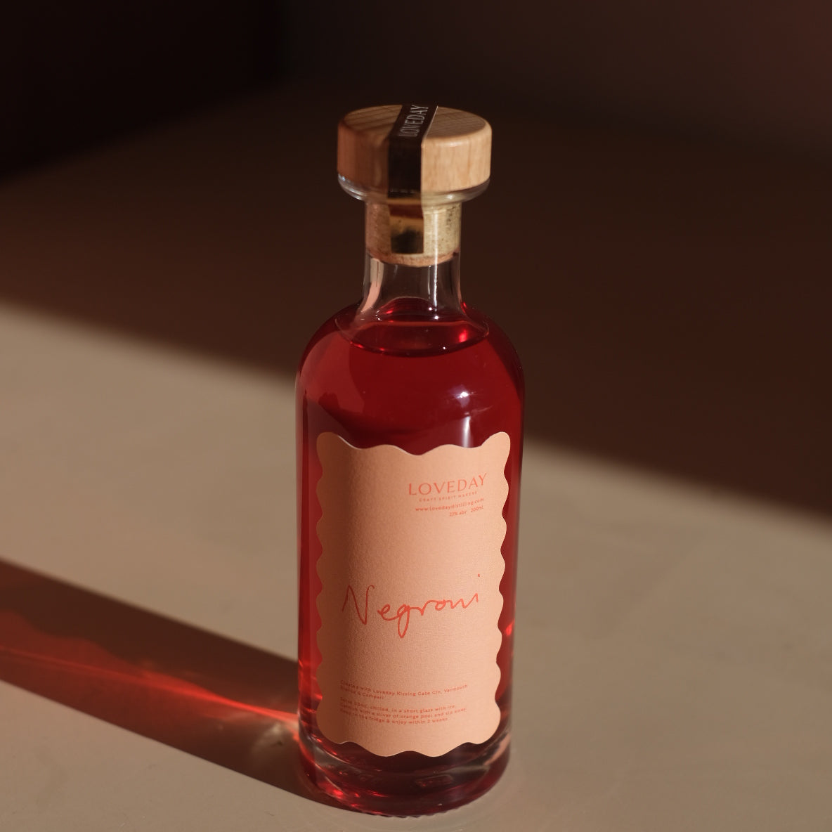 Loveday Distillery Negroni ready-to-pour bottle with ruby red liquid, scalloped peach label, and wooden cork stopper