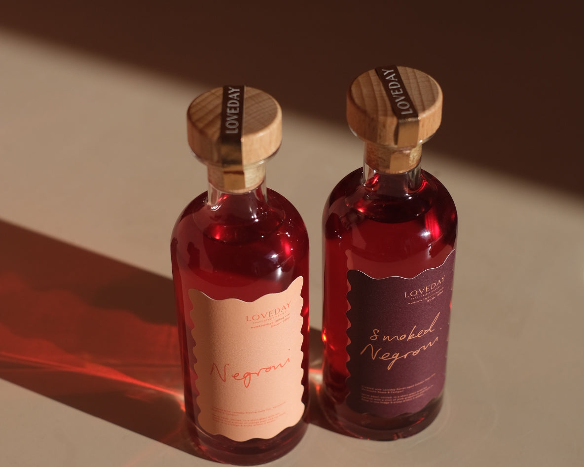 Two Loveday bottled Negroni and Smoked Negroni bottles with wooden stoppers, glowing ruby red in warm directional light